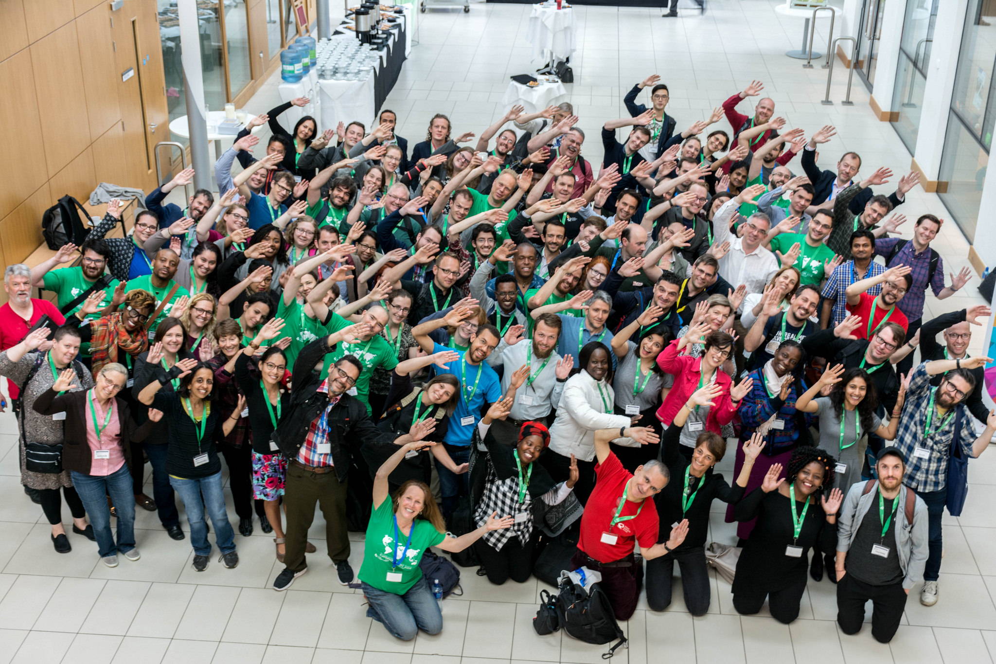Carpentries group shot of > 50 people modelling the carpentries logo by raising their arms and tilting 45 degrees to the left